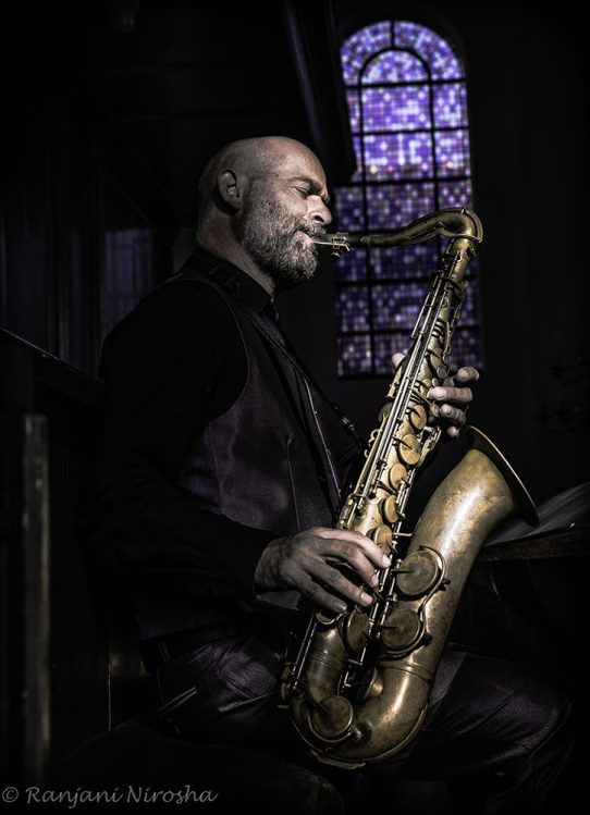 Saxofonist Erwin Benjamins speelt tenorsaxofoon in een kerk met glas-in-loodraam